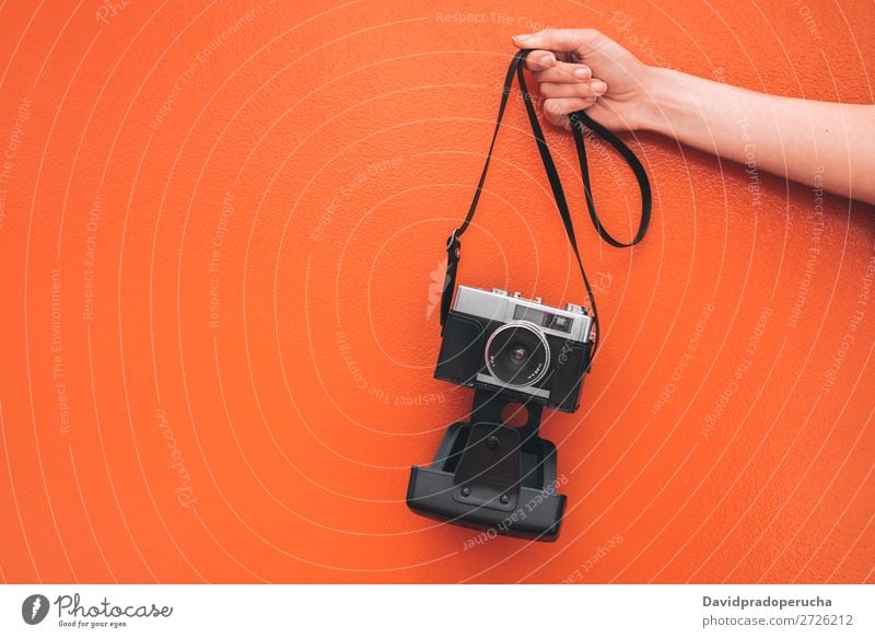 Hand hält eine Vintage-Kamera an der orangefarbenen Wand isoliert. Arme Fotokamera altehrwürdig Orange retro vereinzelt Studioaufnahme Halt Freizeit & Hobby