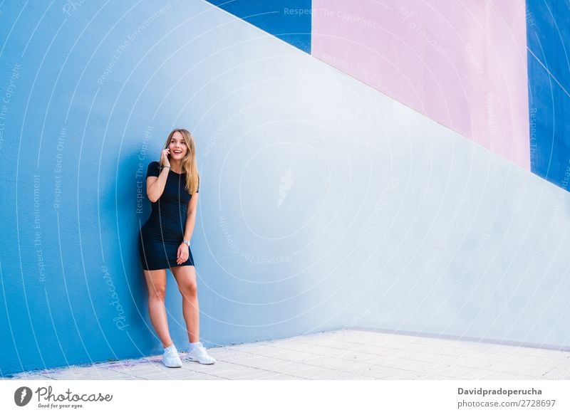Glückliche junge Frau auf dem Handy an einer bunten Wand mehrfarbig blond Telefon Mobile Technik & Technologie Kleid Außenaufnahme Jugendliche Beautyfotografie