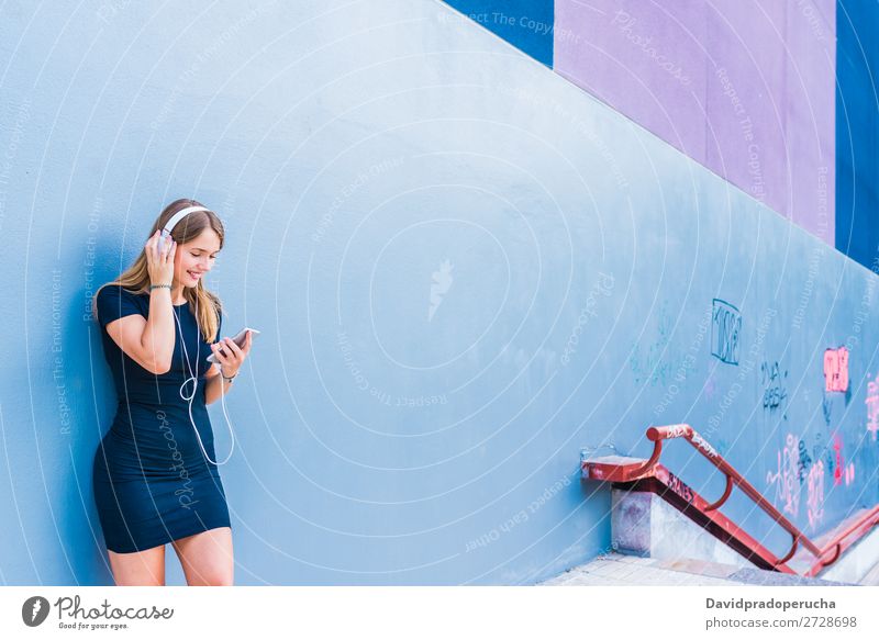 Glückliche junge Frau, die Musik auf dem Handy an einer bunten Wand hört. blond mehrfarbig hören Telefon Mobile Technik & Technologie Kleid Außenaufnahme