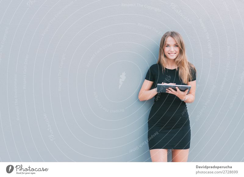 Glückliche junge Frau auf dem Tablett an der Wand vereinzelt blond Tablet Computer Technik & Technologie Kaffee Jugendliche schwarz Kleid Beautyfotografie