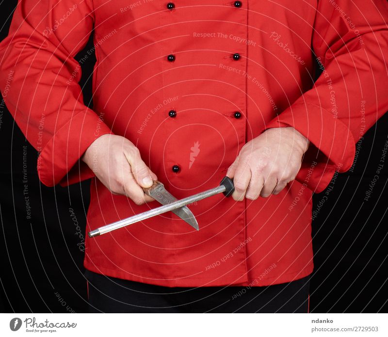 Koch in roter Uniform schärft ein Messer Küche Restaurant Beruf Mensch Mann Erwachsene Hand Stahl stehen schwarz Klinge Kaukasier Küchenchef zerkleinernd