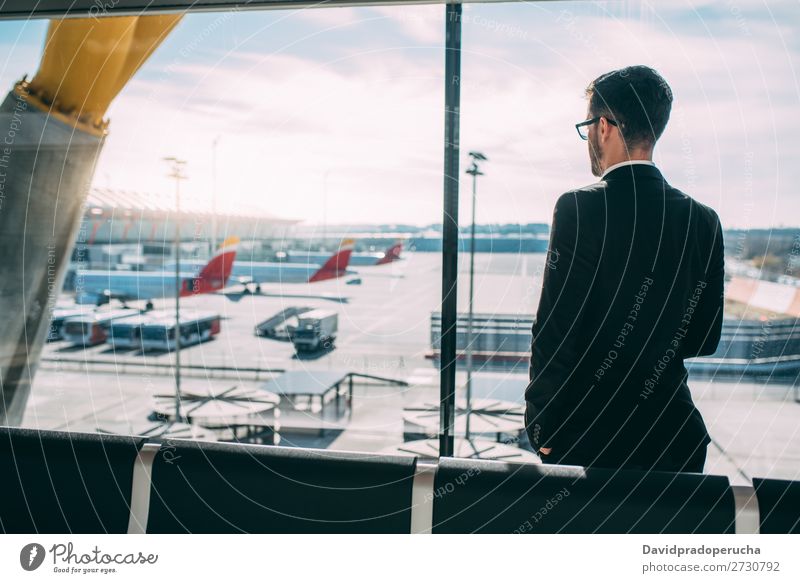 Zurück von einem jungen Geschäftsmann, der mit dem Koffer am Flughafen steht und auf den Flug wartet. Mann Ferien & Urlaub & Reisen Schatten Rücken Business