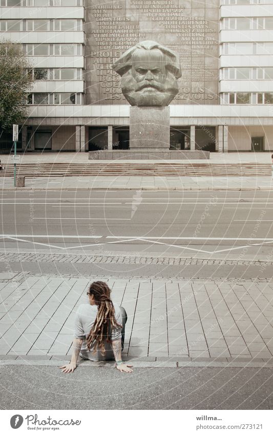 Jugendliche mit Rastas hockt ganz allein lässig am Straßenrand vor dem Denkmal von Karl Marx Marxmonument nachdenken chillen urban Politik Zukunft