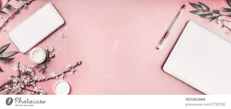 Smartphone und Tablet-PC auf pastellrosa Desktop-Hintergrund mit Kosmetik, Schreibwarengeschirr und weißen Blütenzweigen, Ansicht von oben. Beaut-Blog und weibliches Geschäftskonzept. Flachlegung, Banner