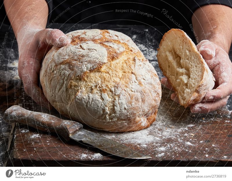 Koch in einer schwarzen Tunika hält frisch gebackenes Brot bereit. Ernährung Tisch Küche Mensch Hand Finger Holz Essen machen dunkel braun weiß Tradition Bäcker