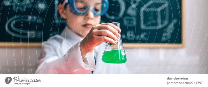 Kleiner Junge Wissenschaftler hält Kolben mit grüner Flüssigkeit gegen von gezeichneten Tafel Flasche Spielen Tisch Wissenschaften Kind Klassenraum Labor