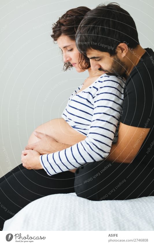Liebevolles schwangeres Paar, das auf dem Bett sitzt. Glück schön Körper Baby Frau Erwachsene Mann Eltern Mutter Vater Familie & Verwandtschaft berühren Lächeln