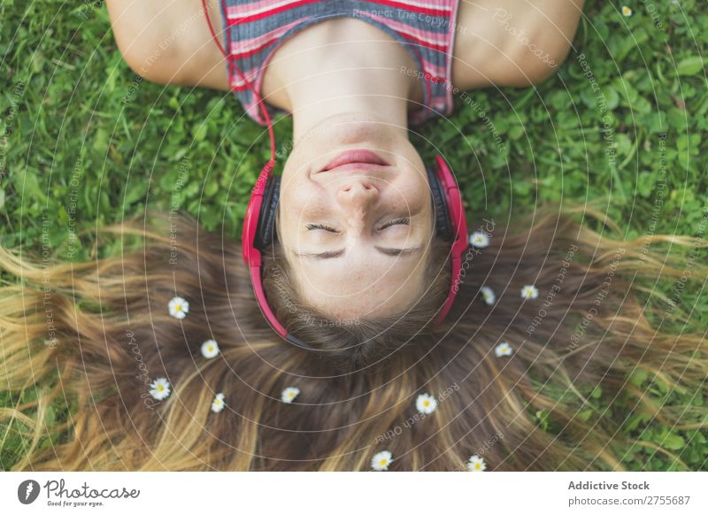 Aufgeregtes Mädchen in Kopfhörern auf Gras Frau expressiv Körperhaltung lügen Park Gesichtsbehandlung Blume Aufregung Model Ausdruck Stil Jugendliche hören