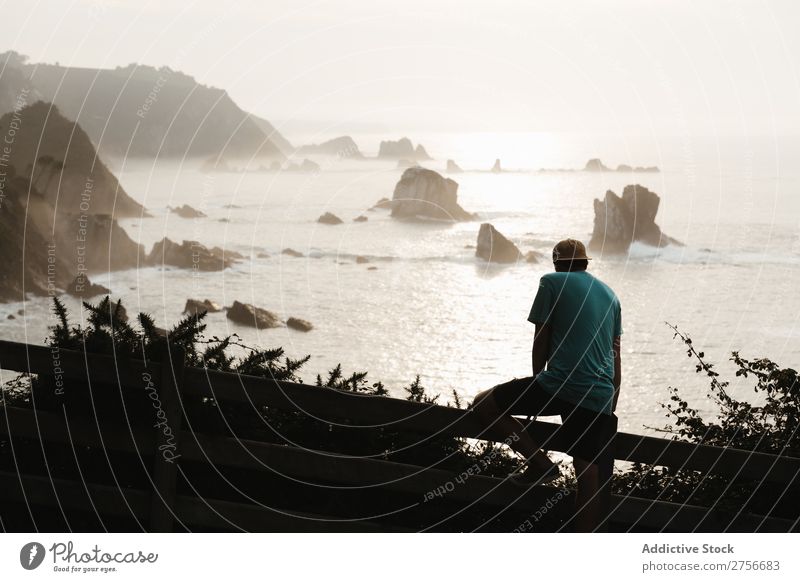 Mann sitzt auf einem Zaun an einer Felsküste. Klippe Meer Felsen Ferien & Urlaub & Reisen Tourismus Natur Landschaft Küste Wasser Sonne Freiheit Stein natürlich