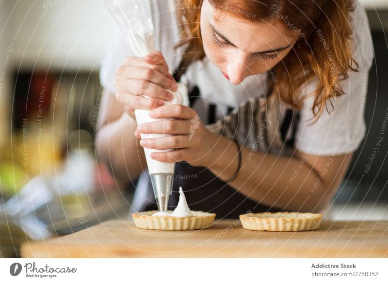 Frau, die Sahne auf Törtchen legt. Dessert kochen & garen Creme Koch Backwarenbeutel Schaumgebäck Küche Lebensmittel süß Rezept heimwärts Vorbereitung backen