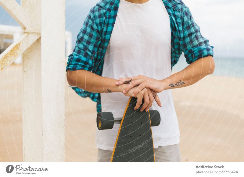Mann in Sommerkleidung hält Skateboard am Sandstrand. Küste Strand Freizeit & Hobby mehrfarbig Youngster Aktion Jugendliche Sport Schlittschuhe Skateboarding