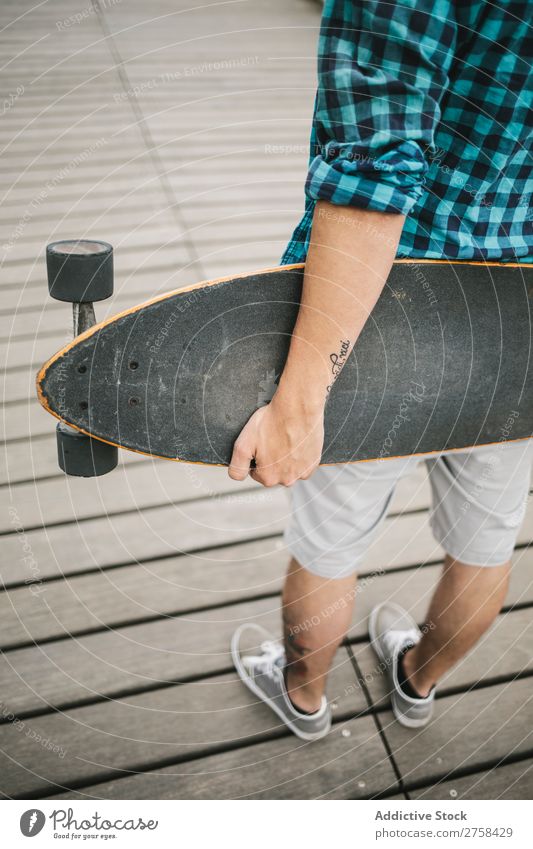 Mann mit Tattoos, der Skateboard an Land hält. Rückansicht. Küste Strand Freizeit & Hobby Sommer mehrfarbig Youngster Aktion Jugendliche Sport Schlittschuhe
