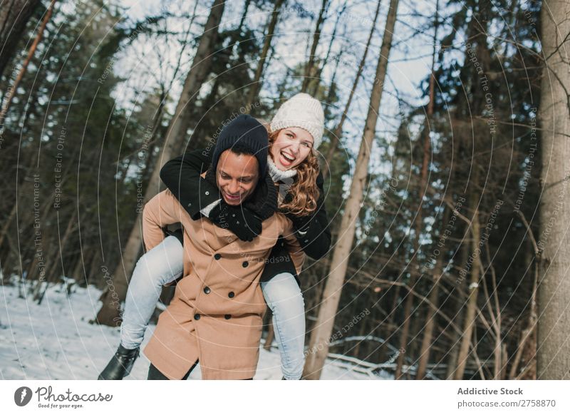Ein Paar mit Spaß im Winterwald multiethnisch Stil warme Kleidung lässig Natur Wald Schnee Huckepack schön Person gemischter Abstammung schwarz Jugendliche