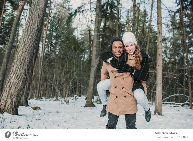 Ein Paar mit Spaß im Winterwald multiethnisch Stil warme Kleidung lässig Natur Wald Schnee Huckepack schön Person gemischter Abstammung schwarz Jugendliche