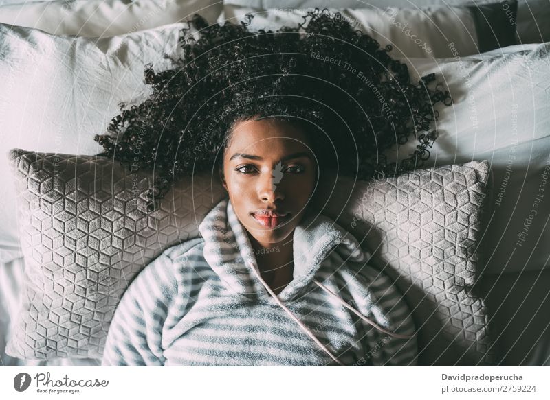 Schöne schwarze Frau mit lockigem Haar, die auf dem Bett liegt und auf die Kamera schaut. Afrikanisch hübsch schön Vogelperspektive Nahaufnahme krause Haare