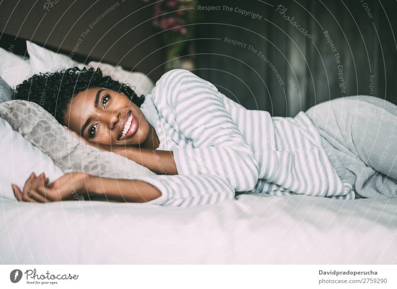 Nahaufnahme einer hübschen schwarzen Frau mit lockigem Haar, die lächelt und auf dem Bett liegt und wegblickt. schwarze Frau Porträt lügen Lächeln Wegsehen
