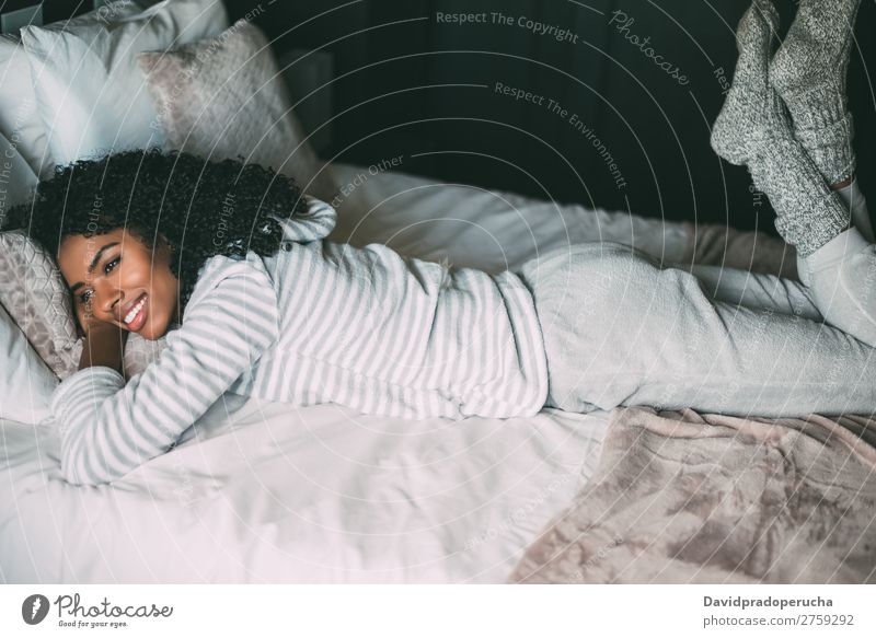 Nahaufnahme einer hübschen schwarzen Frau mit lockigem Haar, die lächelt und auf dem Bett liegt und wegblickt. schwarze Frau Porträt lügen Lächeln Wegsehen