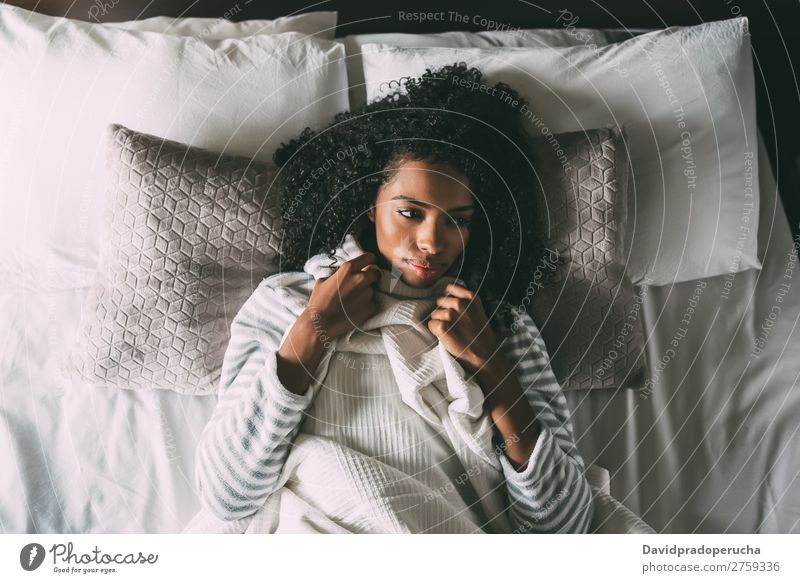 Schöne nachdenkliche schwarze Frau mit lockigem Haar, die auf dem Bett liegt und wegblickt. Fürsorge Afrikanisch hübsch schön Vogelperspektive Nahaufnahme