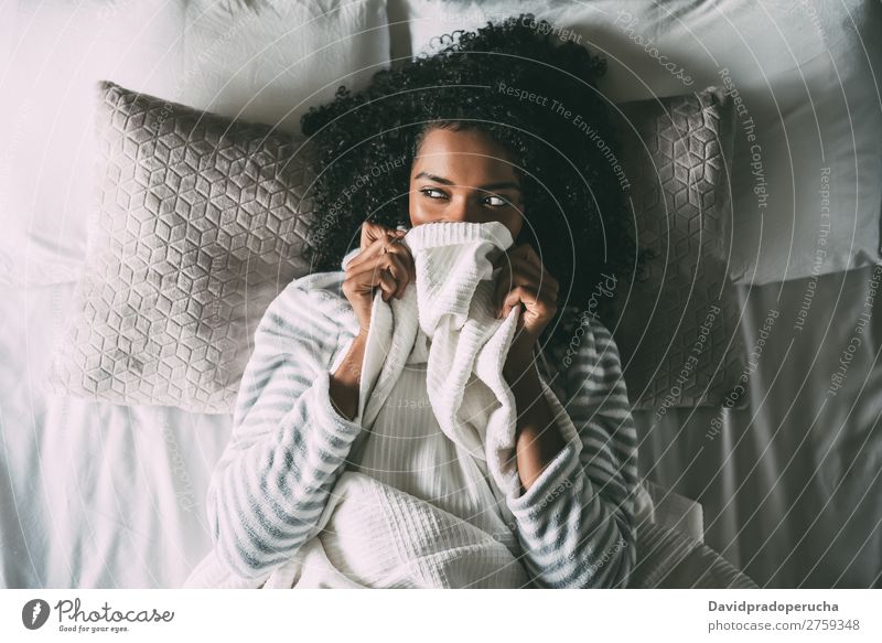 Hübsche schwarze Frau bedeckt ihren Mund mit dem Laken, das wegblickt. Bett Bettlaken deckend Afrikanisch Feldfrüchte hübsch schön Vogelperspektive Nahaufnahme