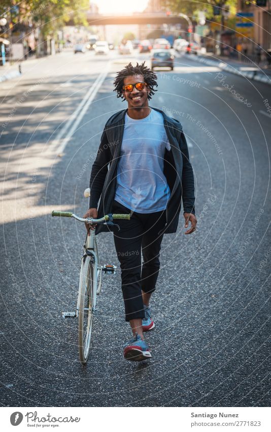 Ein gutaussehender Afro-Mann, der mit seinem Fahrrad unterwegs ist. Jugendliche Afro-Look schwarz Mulatte Afrikanisch Fixie Schickimicki Lifestyle Fahrradfahren