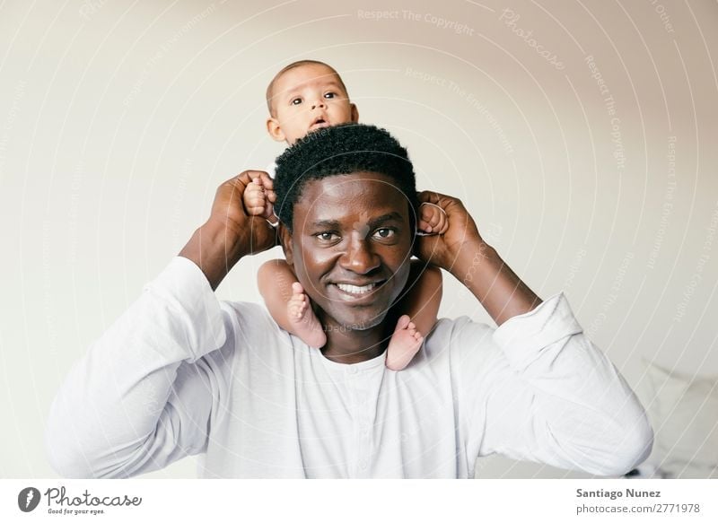 Ein glücklicher Vater huckepack, der sein Baby unterstützt. Junge Kind Kinderbett Mädchen lügen neugeboren Babybett multiethnisch Eltern Hand Afrikanisch