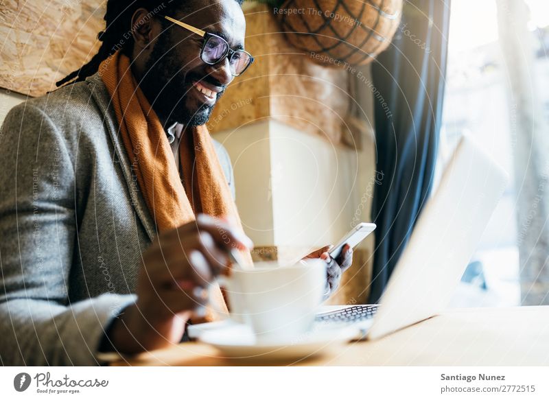 Geschäftsmann mit seinem Laptop im Coffee Shop. Mann schwarz Afrikanisch Amerikaner Business Handy Jugendliche Notebook Computer Coffee-Shop Kaffee Büro Mensch