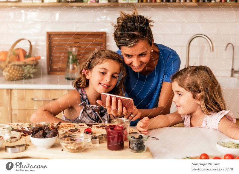 Kleine Schwestern kochen mit ihrer Mutter in der Küche. Kind Mädchen kochen & garen Koch Schokolade Mobile PDA benutzend App Solarzelle Rezept Tochter Tag Glück
