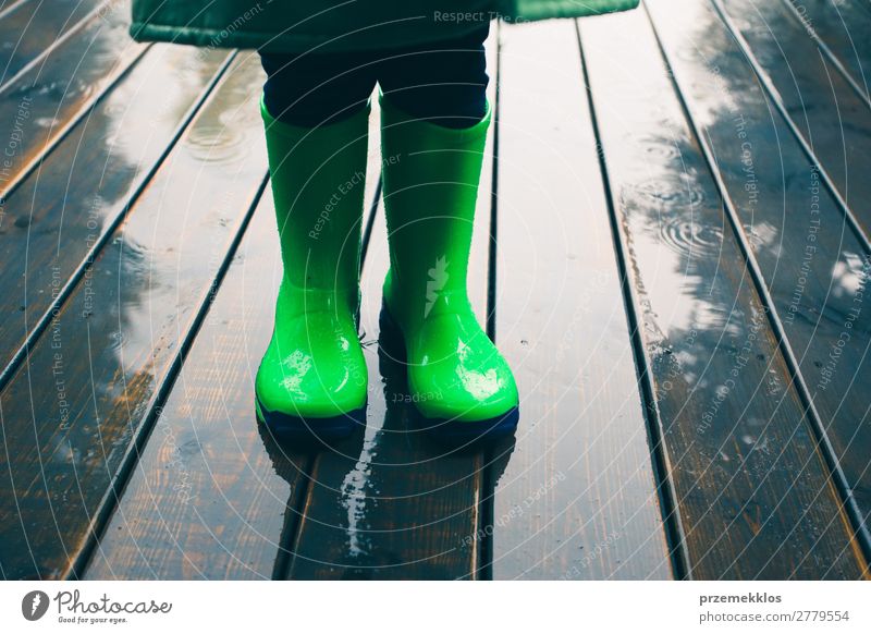 Kind steht auf einer Veranda und trägt grüne Gummistiefel und Regenmantel. Freude Sommer Mensch Junge Wetter Mantel Schuhe Stiefel klein nass niedlich kariert