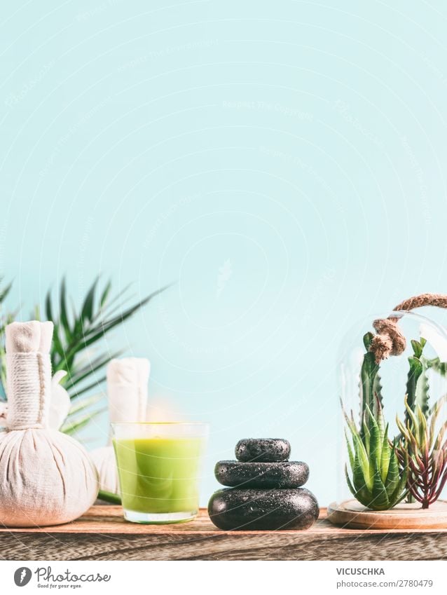 Spa-Hintergrund mit Massagegeräten: Stapel von Massagesteinen, Aromatherapiekerzen, Kräuterstempel auf Holztisch mit Sukkulentenpflanzen auf hellblauem Hintergrund. Wellness-Behandlung
