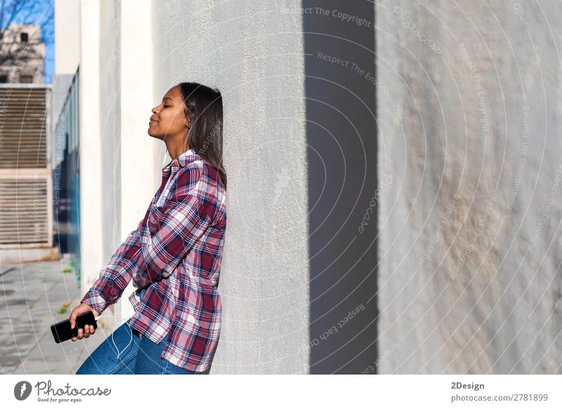 Schöne junge afroamerikanische Frau, die sich an eine weiße Wand lehnt. Lifestyle Stil schön Musik Telefon PDA Mensch feminin Junge Frau Jugendliche Erwachsene