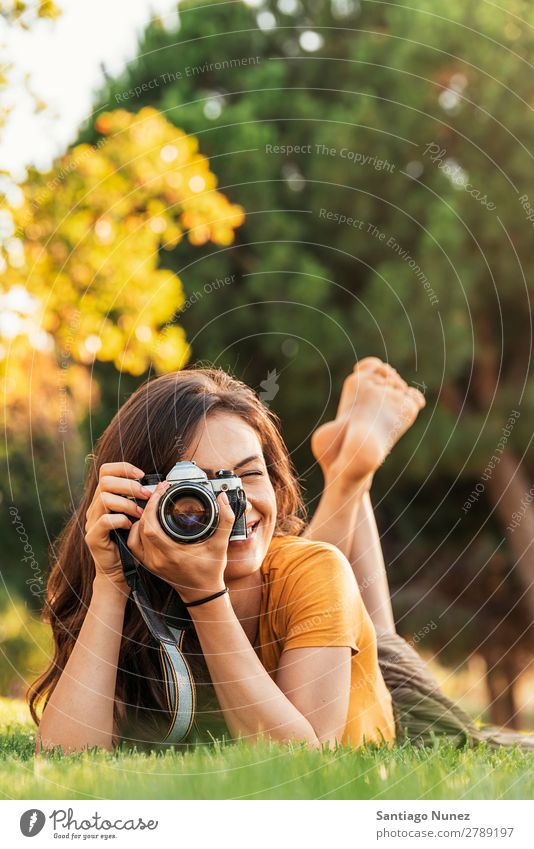 Lächelnde junge Frau, die eine Kamera benutzt, um im Park zu fotografieren. Fotograf Fotografie Fotokamera Jugendliche Mädchen digital weiß Freizeit & Hobby 1