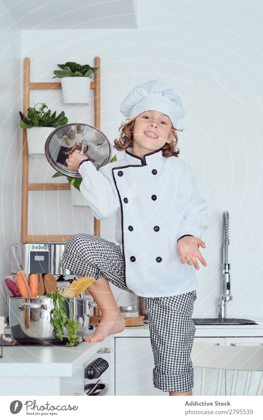 Junge mit Kochmütze mit Deckel neben dem Topf auf Stuhl in der Küche überdeckt Küchenchef Kind Gemüse Hut kochen & garen modern lustig heimwärts Licht