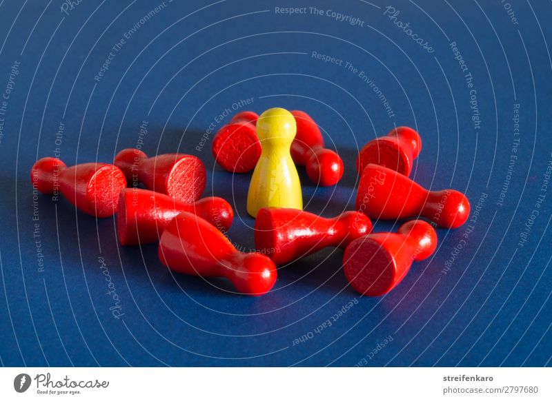 Eine gelbe Spielfigur steht inmitten von vielen roten liegenden Spielfiguren auf blauem Untergrund Wirtschaft Menschengruppe Spielzeug Holz sprechen fallen