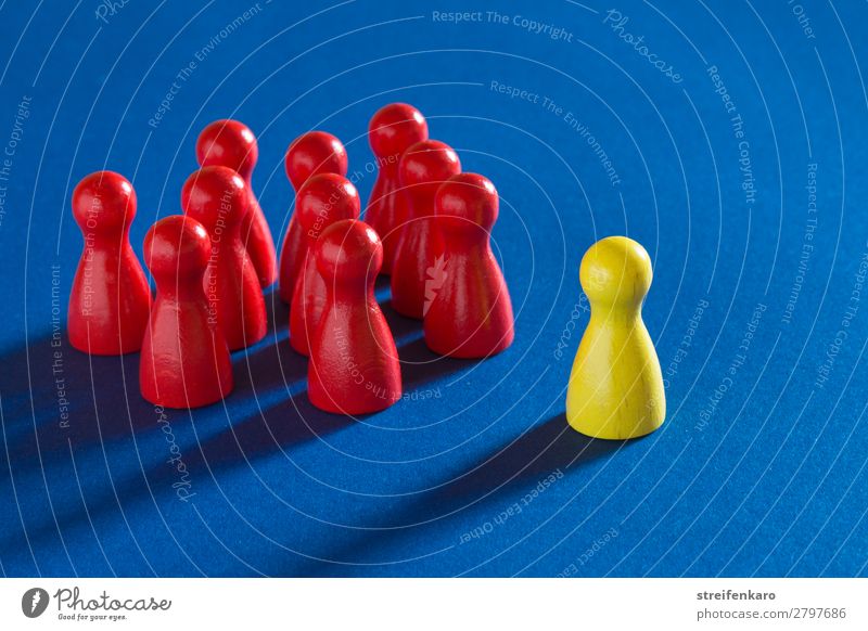 Eine gelbe Spielfigur steht vor einer Gruppe von roten Spielfiguren auf blauem Untergrund lernen Wirtschaft Business Karriere Erfolg sprechen Team