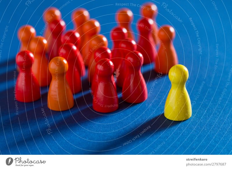 Eine einzelne gelbe Spielfigur steht gegenüber einer Gruppe von roten Spielfiguren auf blauem Untergrund lernen Berufsausbildung Wirtschaft Business Karriere
