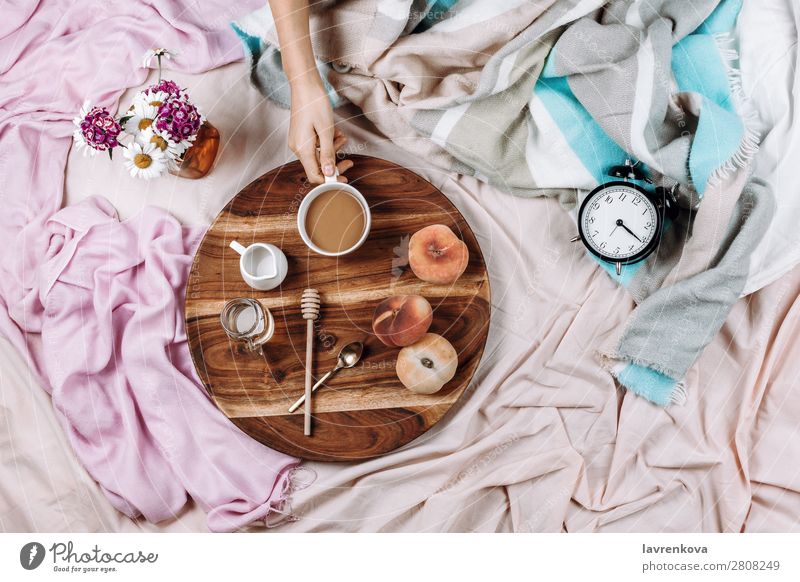 Gemütliches Flachbett aus Holztablett mit Tasse Kaffee, Pfirsichen, Kaffeesahne und Sahne. Wecker Morgen Becher Flachlegung flache Verlegung Schlafzimmer
