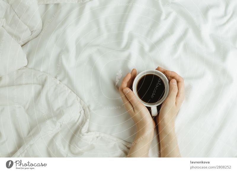 Frauenhände halten Tasse Kaffee im Bett auf weißen Laken. Winter Herbst Getränk flache Verlegung Bettlaken Lifestyle weich Becher Hand Wärme Geborgenheit