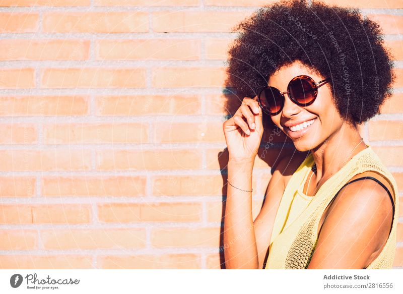 Junge schöne afroamerikanische Frau, die posiert und lächelt, während sie an der Ziegelwand steht. Afrikanisch Amerikaner charmant Backstein Model Hand