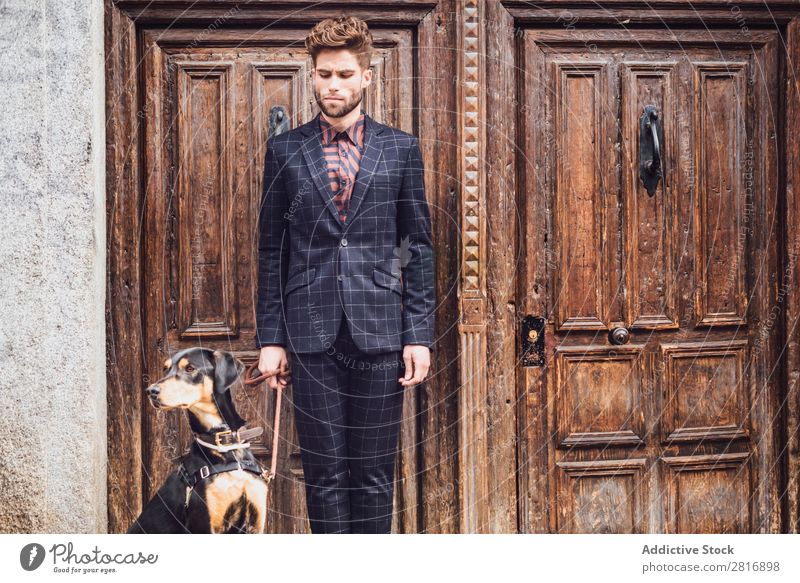Schöner eleganter junger Modemann im trendigen Kostümanzug mit Hund, alter Holztürhintergrund Anzug Mann Herr modisch Bekleidung Stil Model Hemd Hand lässig