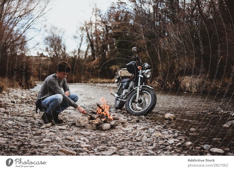 Reisender, der Lagerfeuer hält Mann Feuerstelle Motorrad Einsamkeit Expedition Flamme Brennholz Fernweh Aktion Abenteuer reisend Tourismus wandern Verkehr