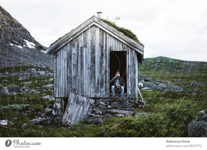 Ein Mann sitzt in einem alten Haus in der Natur. Hütte Berge u. Gebirge abgelegen ruhig Gelände Biegen aber Landschaft friedlich Gebäude Außenseite Idylle