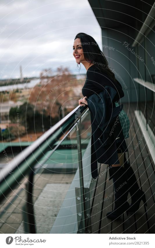 Fröhliche Frau am Handlauf stehend hübsch Jugendliche schön heiter Lächeln Balkon Gebäude modern Zeitgenosse brünett attraktiv Mensch Beautyfotografie