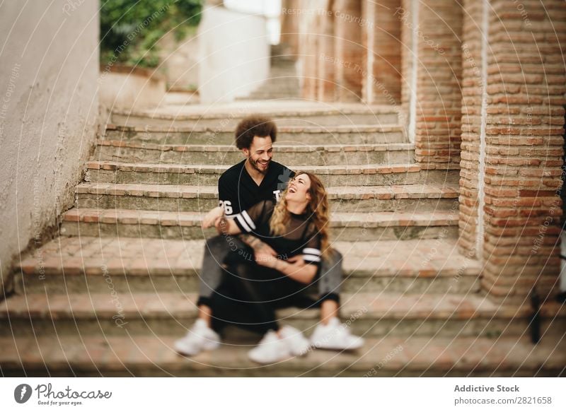 Ein Paar lacht, während es sich an den Stufen in der Stadt umarmt. lachen Spaß haben Porträt Straße sitzen Zusammensein Umarmen Freitreppe ländlich Treppe