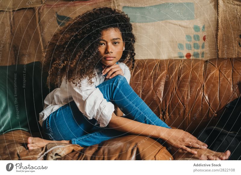Stilvolle ethnische Frau auf der Couch hübsch schön urwüchsig schwarz lockig Jugendliche Leder Liege Sofa braun sitzen Blick in die Kamera brünett attraktiv