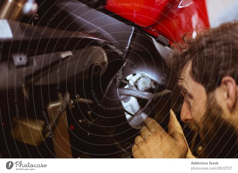 Mann benutzt Licht, um ins Fahrrad zu schauen. Mitarbeiter Mensch Blick inspizierend Motorrad Werkstatt geparkt Verkehr Fahrzeug Garage benutzerdefiniert