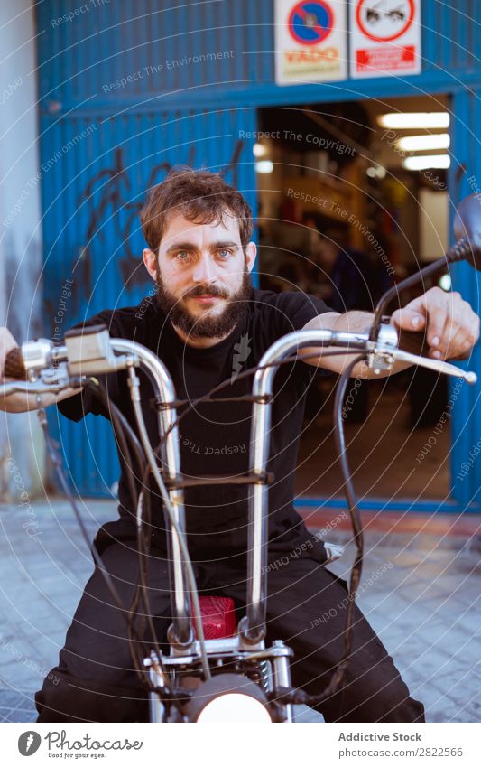 Mann auf dem Fahrrad in der Garage Motorradfahren Blick in die Kamera Porträt Mensch bärtig Werkstatt geparkt Verkehr Fahrzeug benutzerdefiniert