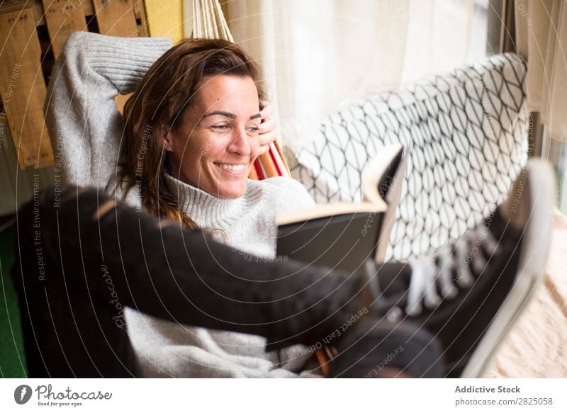 Fröhliche Frau liegend mit Buch heimwärts Erholung lügen Hängematte lesen heiter Lächeln Literatur Lifestyle schön Raum Mensch lässig Erwachsene Haus