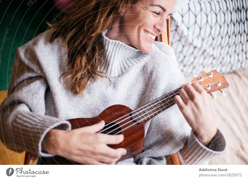 Fröhliche Frau beim Ukulelele spielen heimwärts Erholung Spielen Lifestyle Musiker heiter Lächeln schön Raum Mensch lässig Erwachsene Haus Beautyfotografie