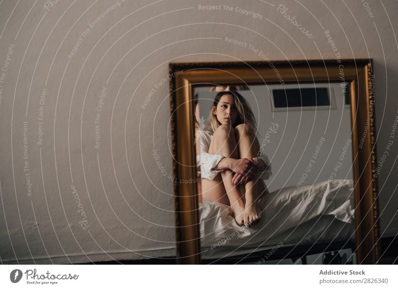 Das Spiegelbild einer Frau, die ihre Knie umarmt und auf einem Bett sitzt. Horizontale Innenaufnahme. umarmend Reflexion & Spiegelung Wegsehen Morgen heimwärts