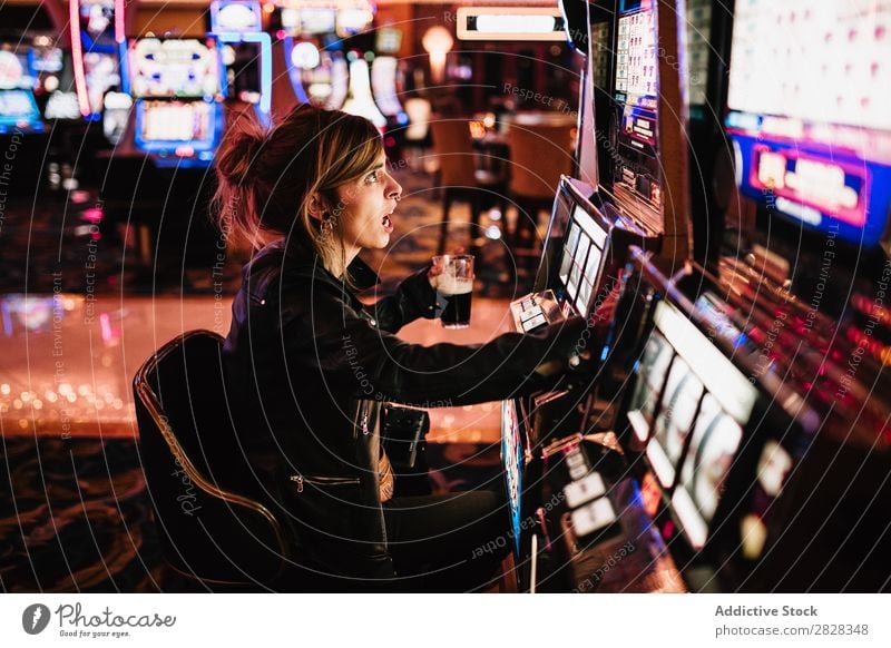 Seitenansicht einer Frau, die im Casino sitzt und am Spielautomaten spielt. Glücksspiel Kurhaus Risiko Spieler Gewinner Spielen Glücksspieler glücklich
